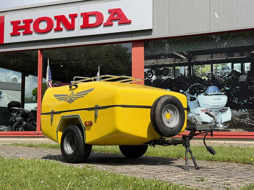 Gelber Anhänger vor einem Honda-Geschäft. Im Hintergrund sind Motorräder zu sehen. Passend für Goldwing Uslar.