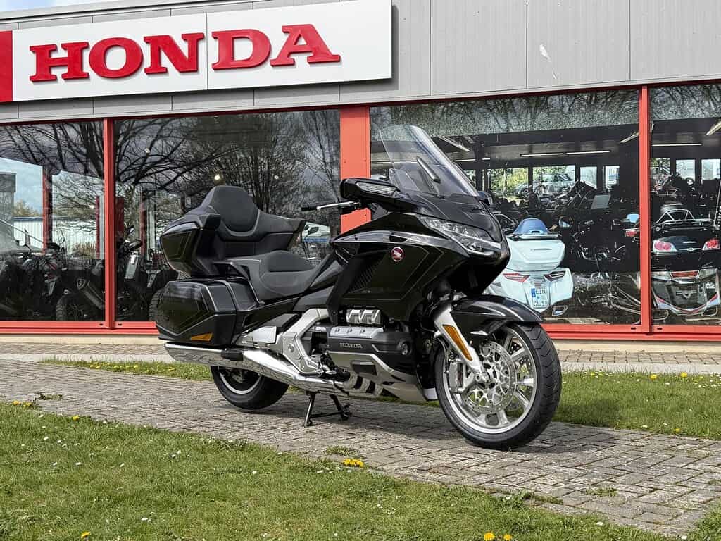 Schwarze Honda Goldwing vor einem Honda Händler. Gebäude mit großem Honda-Logo im Hintergrund. Motorräder im Fenster.